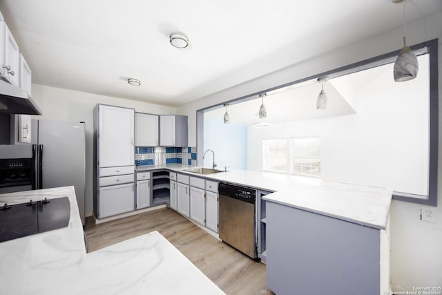 kitchen featuring light wood finished floors, a peninsula, a sink, pendant lighting, and dishwasher