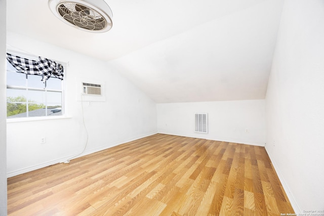 additional living space with a wall unit AC, light wood-type flooring, vaulted ceiling, baseboards, and visible vents