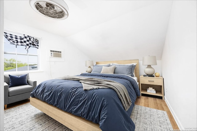 bedroom featuring light wood-style floors, lofted ceiling, an AC wall unit, and baseboards