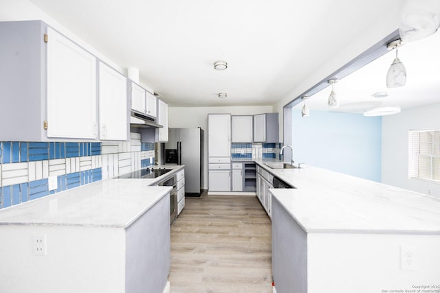 kitchen featuring a peninsula, a sink, tasteful backsplash, black electric stovetop, and under cabinet range hood