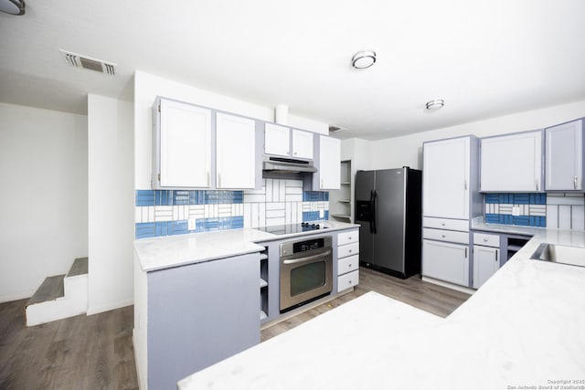 kitchen with light wood-style floors, stainless steel appliances, light countertops, under cabinet range hood, and visible vents
