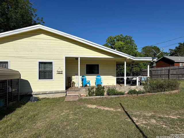 back of property with a lawn, fence, and covered porch