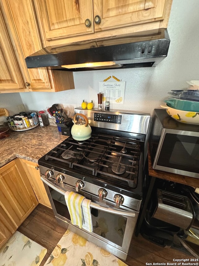 kitchen with dark wood-type flooring, appliances with stainless steel finishes, under cabinet range hood, and dark countertops