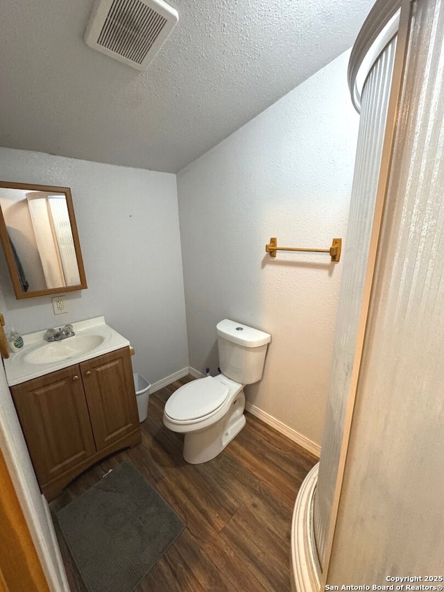 half bath featuring visible vents, wood finished floors, vanity, baseboards, and toilet