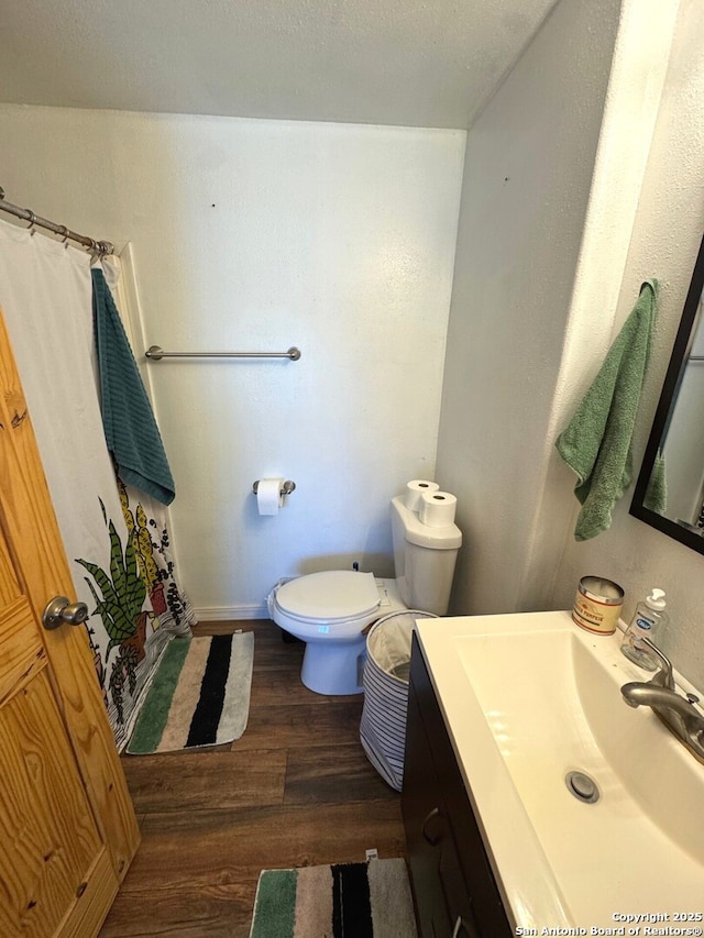 bathroom featuring vanity, toilet, baseboards, curtained shower, and wood finished floors