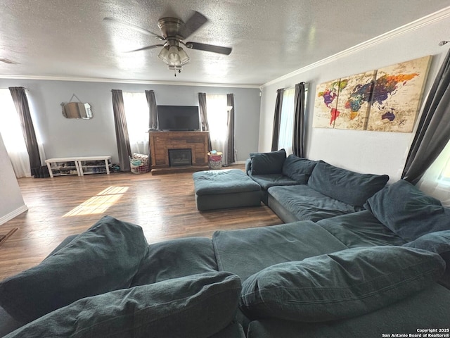 living area with crown molding, wood finished floors, a fireplace, a textured ceiling, and a ceiling fan