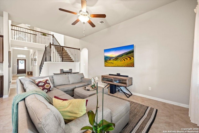 living area featuring arched walkways, baseboards, visible vents, stairs, and ceiling fan