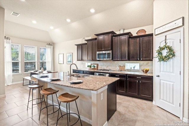 kitchen with vaulted ceiling, a sink, an island with sink, a breakfast bar area, and stainless steel appliances