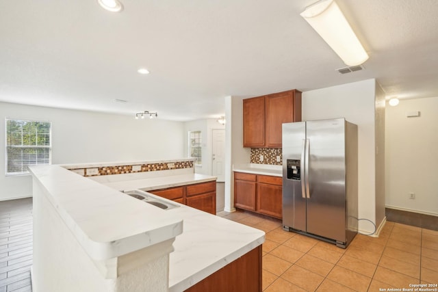 kitchen with tasteful backsplash, light tile patterned floors, brown cabinets, a sink, and stainless steel refrigerator with ice dispenser