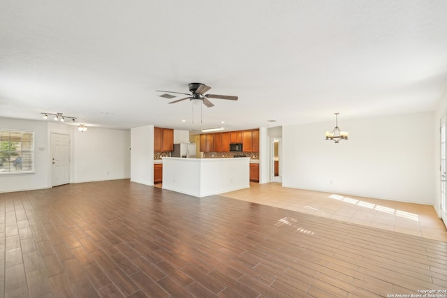 unfurnished living room with light wood-style flooring, visible vents, ceiling fan with notable chandelier, and baseboards
