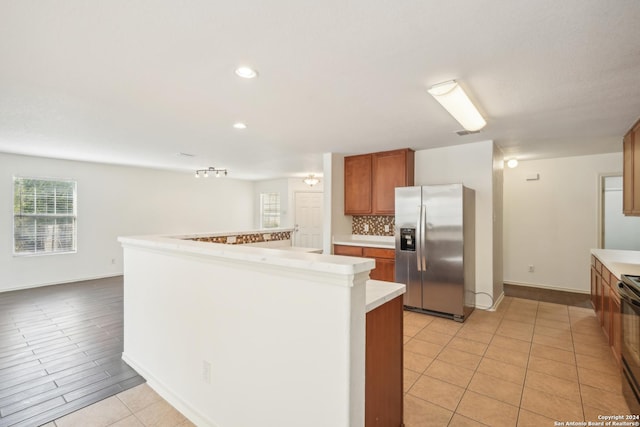 kitchen with stainless steel refrigerator with ice dispenser, backsplash, brown cabinetry, and light countertops