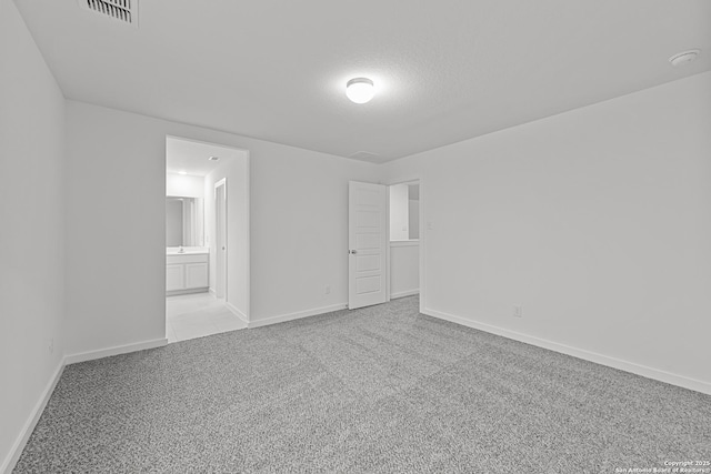 unfurnished bedroom with connected bathroom, visible vents, light carpet, and baseboards