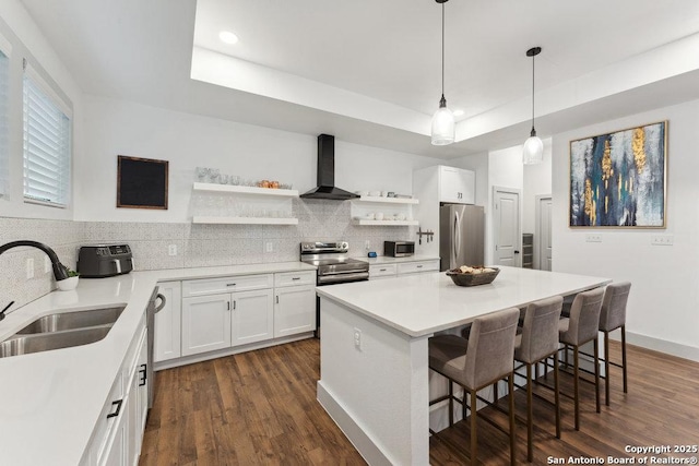 kitchen featuring wall chimney range hood, open shelves, a sink, a raised ceiling, and appliances with stainless steel finishes