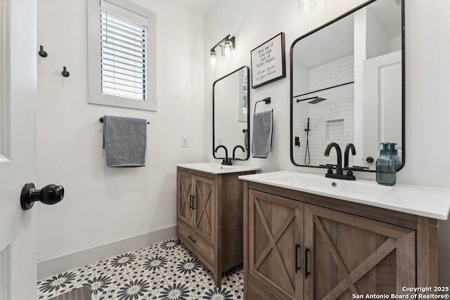 full bathroom with two vanities, baseboards, tiled shower, and a sink