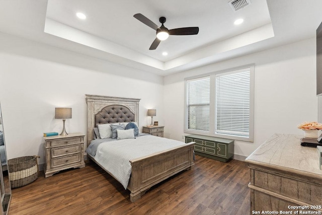 bedroom with a tray ceiling, visible vents, dark wood-type flooring, and recessed lighting
