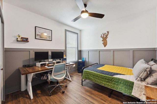 bedroom with wood finished floors, a decorative wall, a wainscoted wall, and a ceiling fan