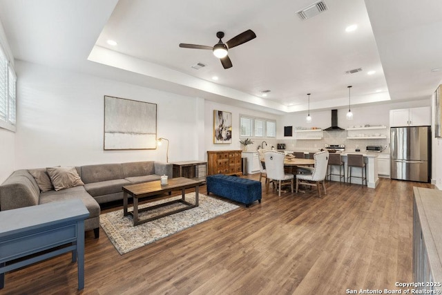 living area with wood finished floors, a ceiling fan, visible vents, and a raised ceiling