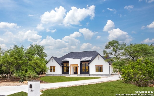 modern inspired farmhouse featuring stucco siding, a standing seam roof, and a front yard