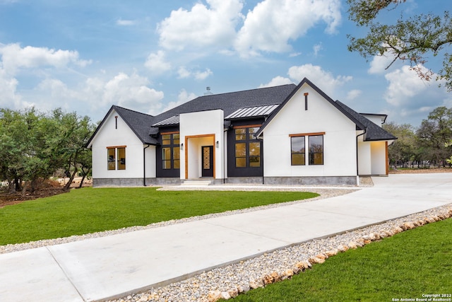 modern farmhouse style home featuring concrete driveway, a front lawn, metal roof, stucco siding, and a standing seam roof