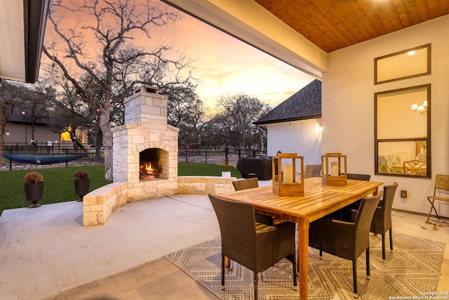 patio terrace at dusk with outdoor dining area, fence, and an outdoor stone fireplace