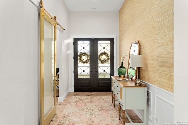 entryway with a barn door, an accent wall, wainscoting, french doors, and light wood finished floors