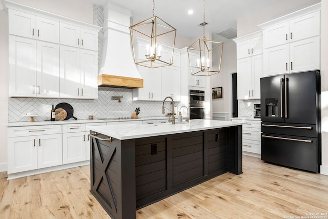 kitchen featuring tasteful backsplash, an inviting chandelier, premium range hood, white cabinets, and black fridge