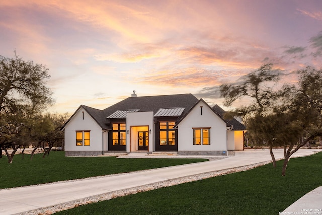 view of front of house with a standing seam roof, a front lawn, driveway, a chimney, and stucco siding