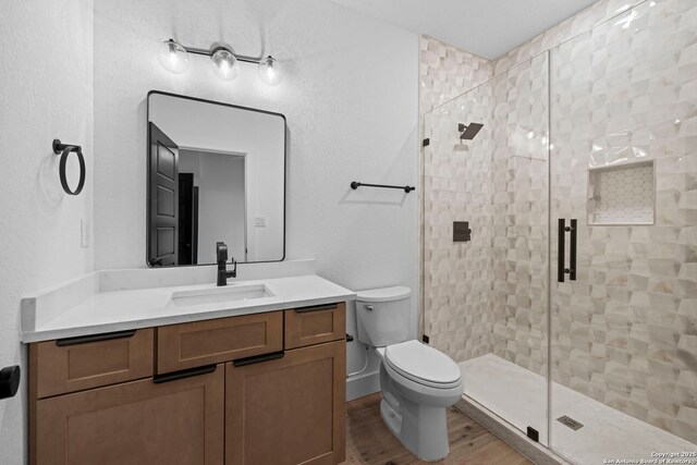 bathroom with a shower stall, toilet, vanity, and wood finished floors