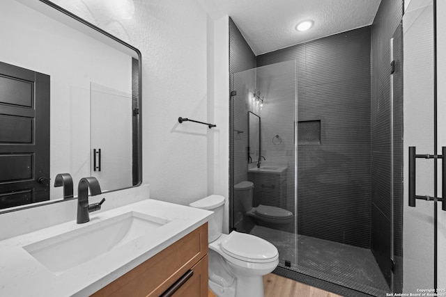 bathroom featuring a shower stall, wood finished floors, a textured ceiling, vanity, and toilet