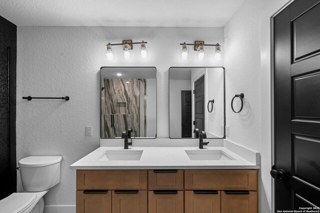 full bath featuring toilet, a textured wall, a sink, and double vanity