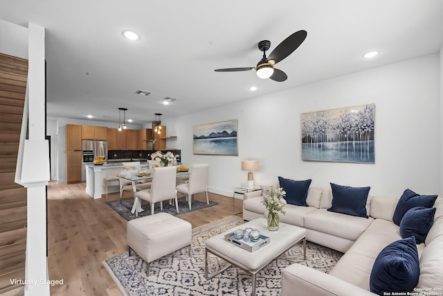 living room with a ceiling fan, light wood-style flooring, stairs, and recessed lighting