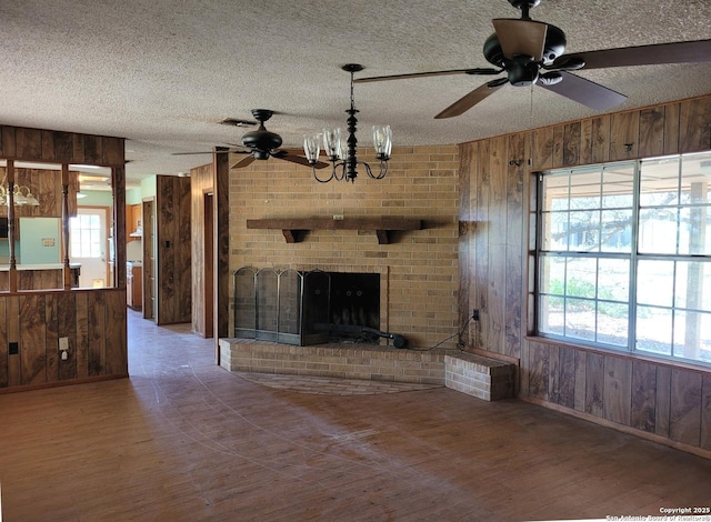 unfurnished living room with a fireplace, wood walls, a textured ceiling, wood finished floors, and ceiling fan with notable chandelier