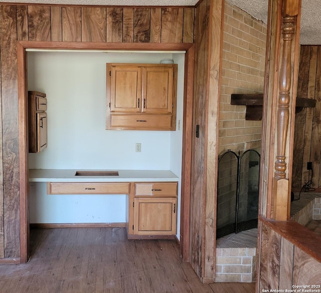 interior space featuring a brick fireplace, built in study area, light countertops, a textured ceiling, and wood finished floors
