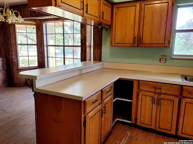 kitchen featuring brown cabinetry, wood finished floors, a notable chandelier, and light countertops