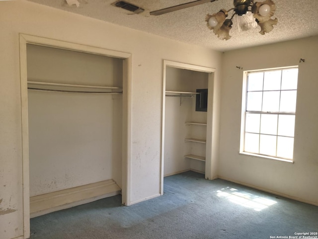 unfurnished bedroom featuring a textured ceiling, ceiling fan, visible vents, carpet floors, and multiple closets