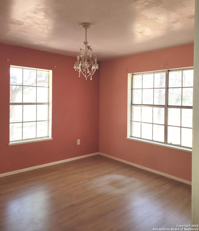 empty room with baseboards, wood finished floors, and a chandelier