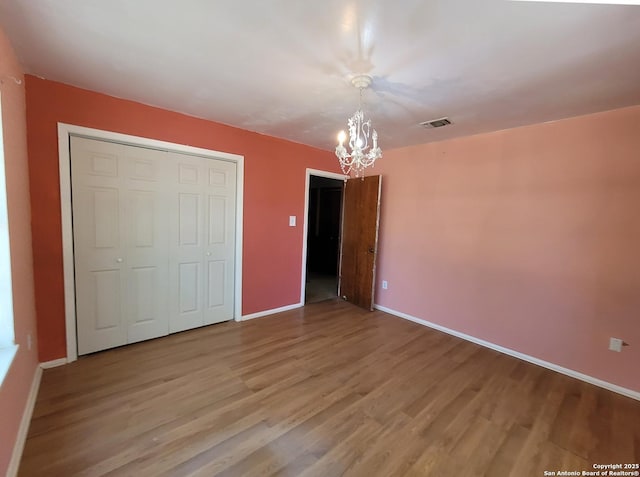 unfurnished bedroom with an inviting chandelier, wood finished floors, visible vents, and baseboards