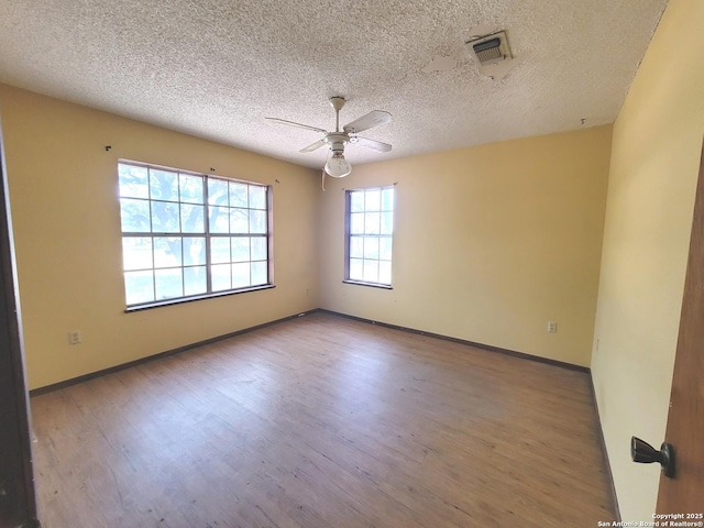 empty room featuring ceiling fan, visible vents, baseboards, a textured ceiling, and wood finished floors
