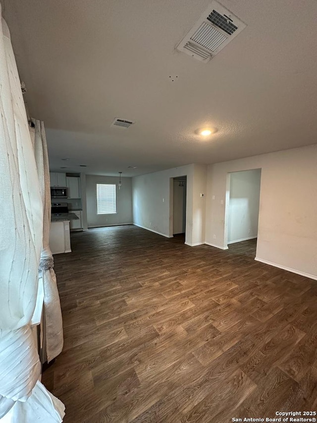 unfurnished living room with baseboards, visible vents, and dark wood-style floors