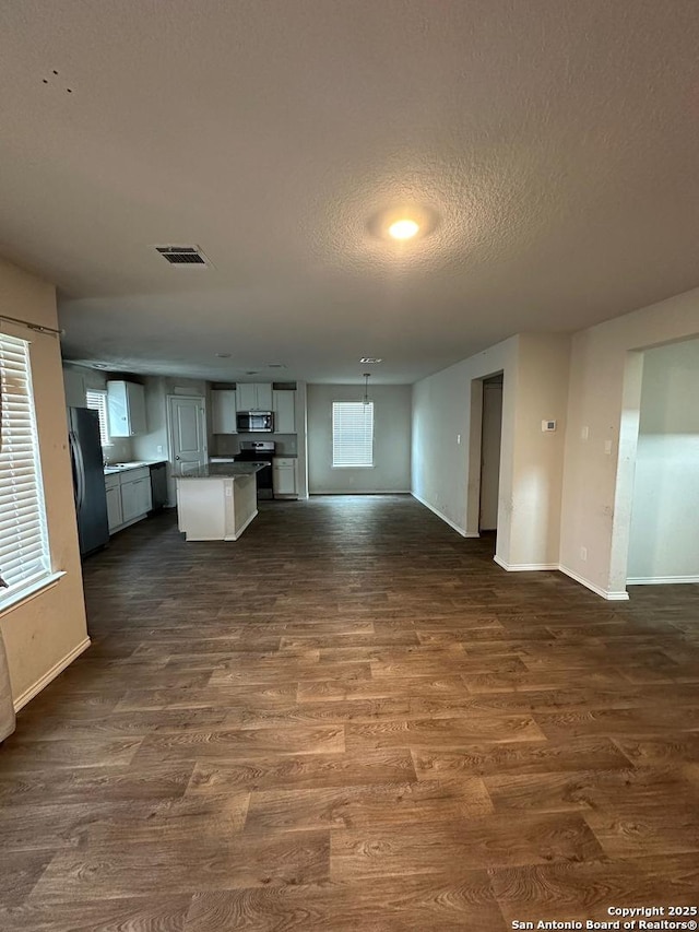 unfurnished living room with baseboards, visible vents, and dark wood-type flooring