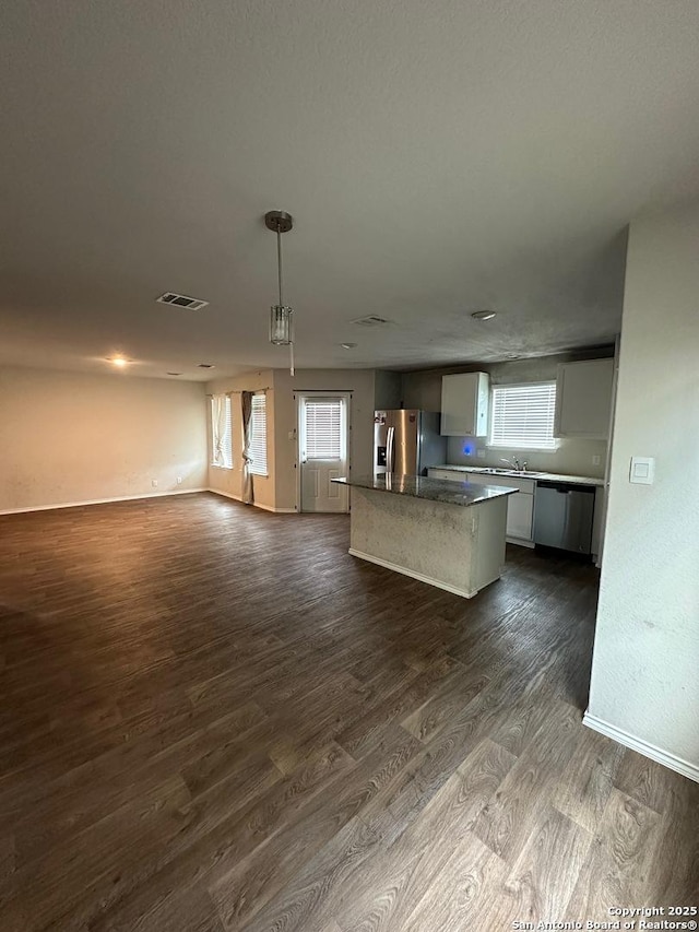 kitchen with open floor plan, dark wood finished floors, appliances with stainless steel finishes, visible vents, and a kitchen island