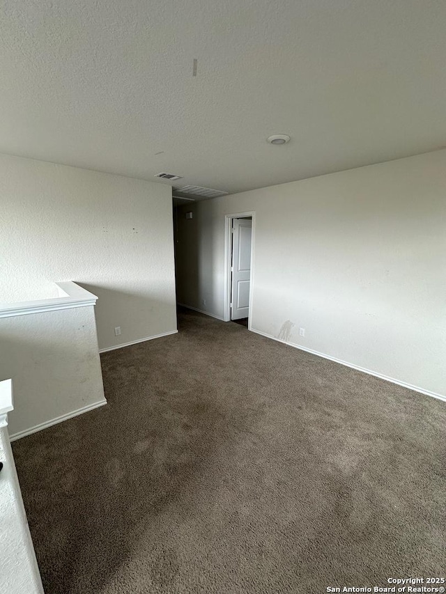 empty room with dark carpet, baseboards, a textured ceiling, and visible vents