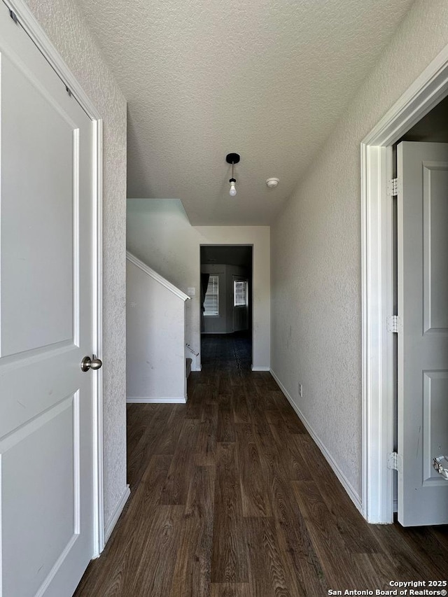 corridor with wood finished floors, a textured ceiling, baseboards, and a textured wall