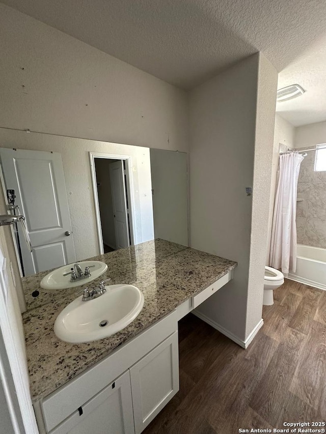 full bath with wood finished floors, a textured ceiling, vanity, toilet, and visible vents