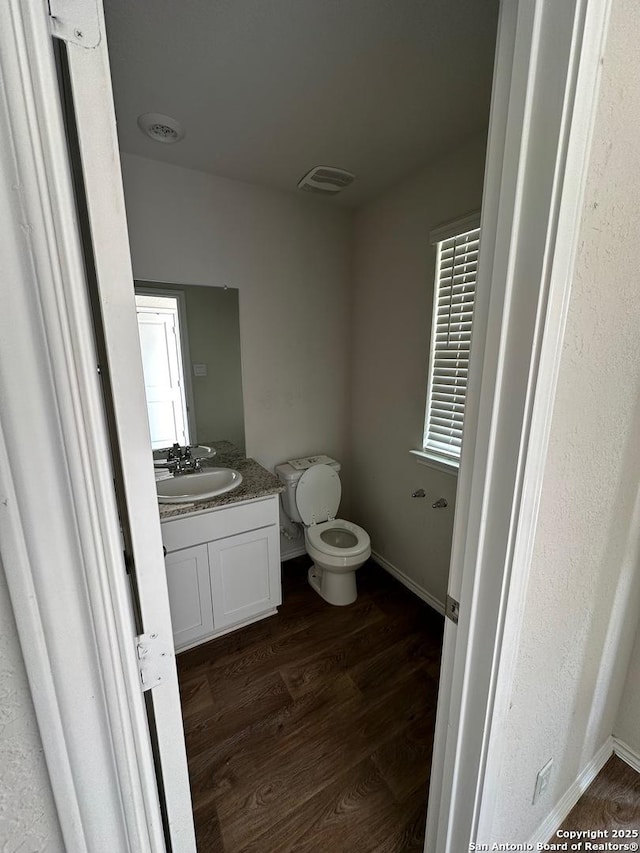 half bath with baseboards, wood finished floors, vanity, and toilet