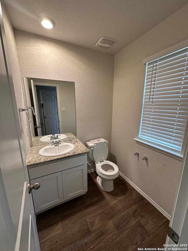 half bathroom with wood finished floors, visible vents, toilet, vanity, and a textured ceiling
