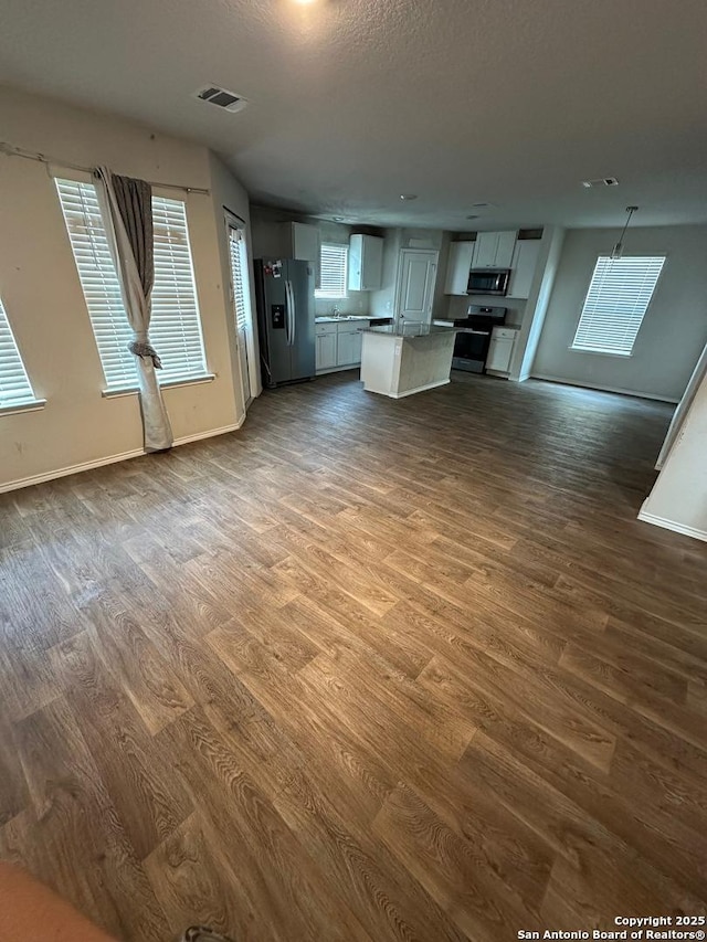 unfurnished living room with baseboards, dark wood-type flooring, and visible vents