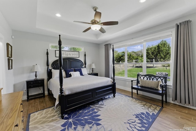 bedroom with light wood-style flooring, a tray ceiling, and multiple windows