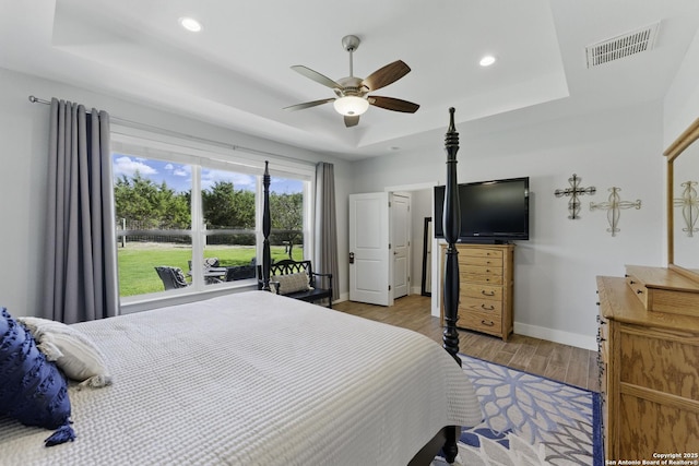 bedroom featuring visible vents, baseboards, wood finished floors, and a tray ceiling