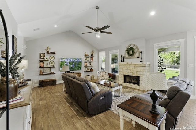 living area with lofted ceiling, wood finished floors, a stone fireplace, and ceiling fan
